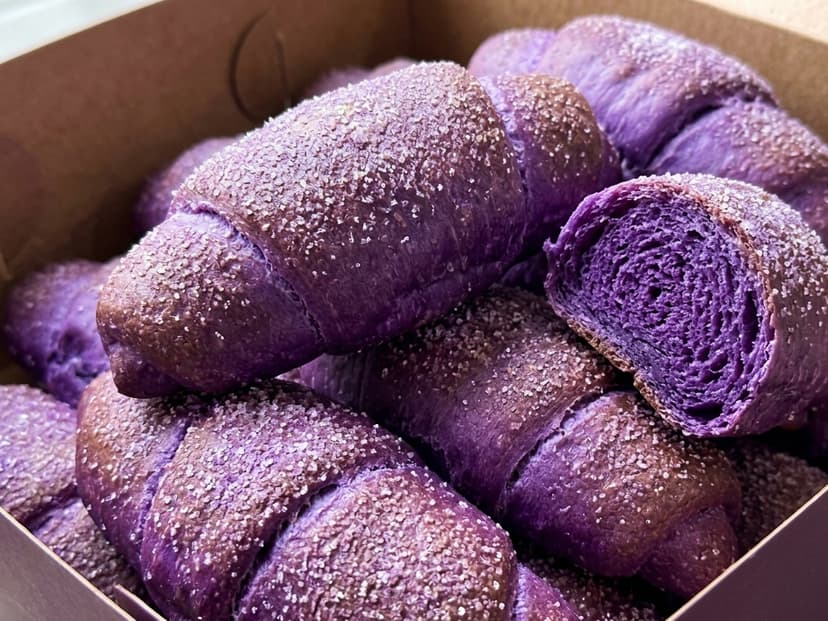 Box of vibrant purple ube señorita rolls with sparkling sugar, one halved to show the spiral purple crumb interior
