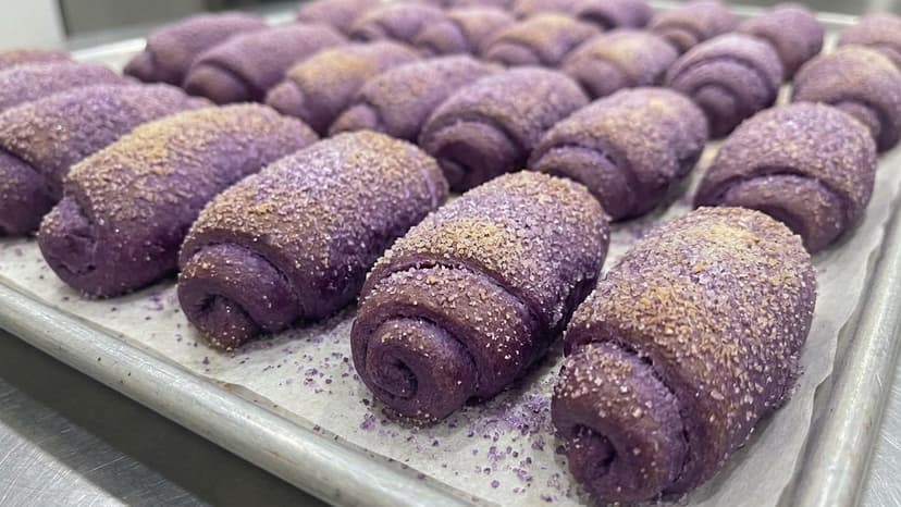 Rows of deep purple ube señorita rolls on a baking tray dusted with sugar crystals
